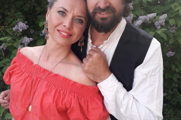 Punaiseen paitaan ja hameeseen pukeutunut nainen nojaa valkoiseen paitaan ja mustaan liiviin pukeutuneeseen mieheen.