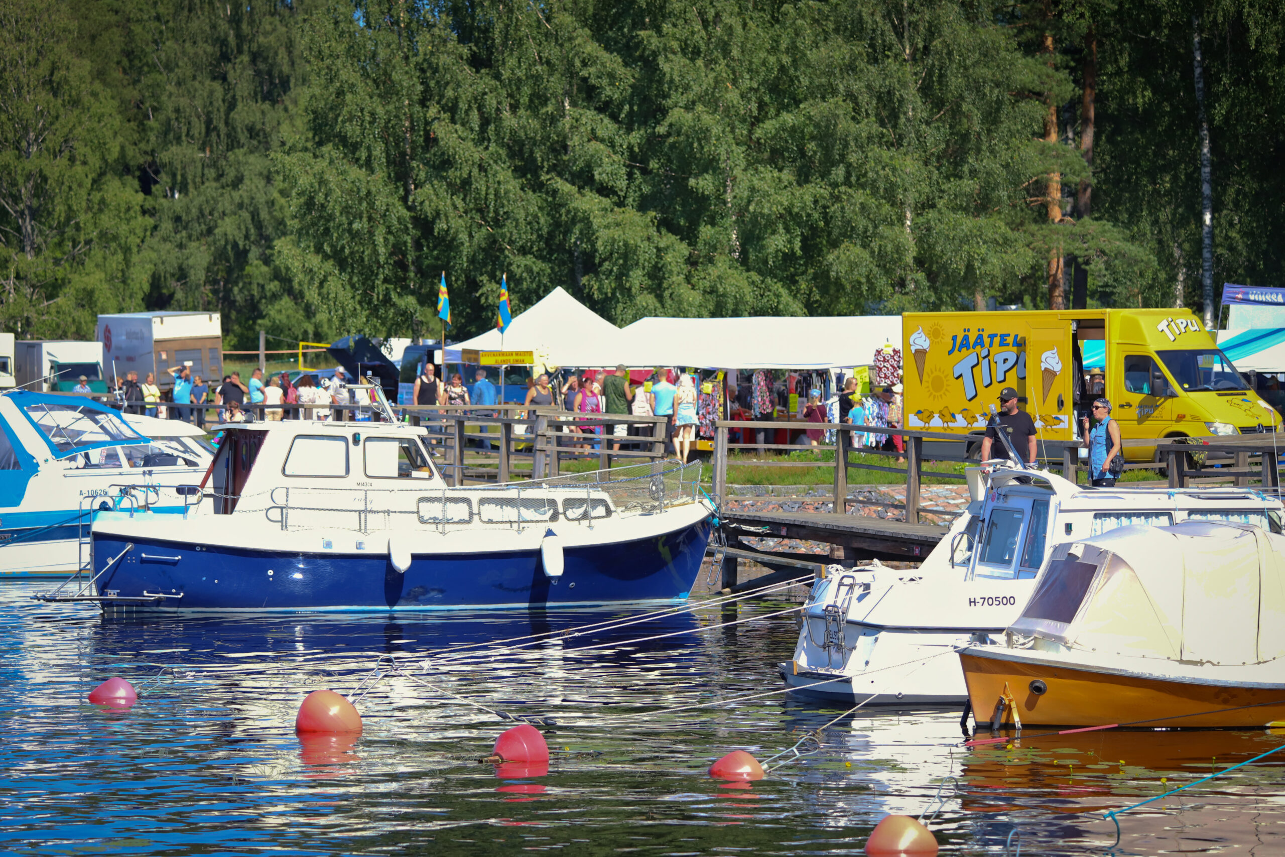 Kesäinen kuva, jossa veneet ovat laiturissa ja torilla on markkinat menossa