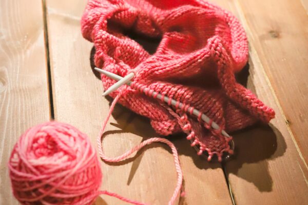 Pinkki keskeneräinen neulostyö puupöydän päällä